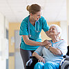 Krankenpflegerin hält Hand von älterer Patientin im Rollstuhl.