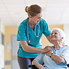 Krankenpflegerin hält Hand von älterer Patientin im Rollstuhl.