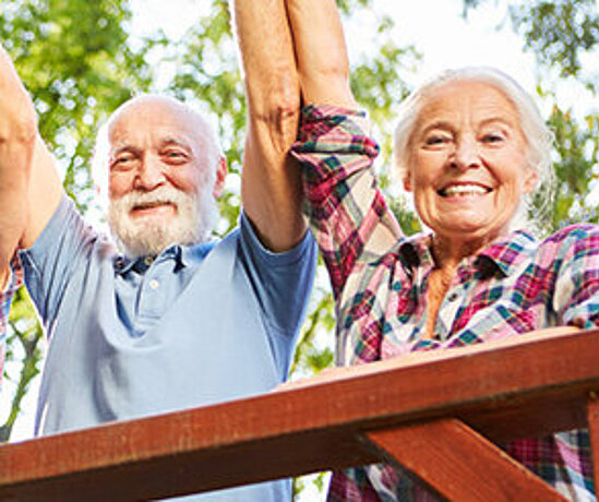 Ein Rentnerpaar streckt freudig die Arme in die Luft.