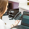 Eine Beschäftigte einer Arztpraxis arbeitet am Laptop hinter dem Empfangstresen.