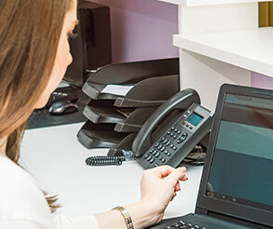 Eine Beschäftigte einer Arztpraxis arbeitet am Laptop hinter dem Empfangstresen.