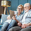 Ein älteres Paar sitzt gemütlich zu Hause auf der Couch und nutzt ein Tablet.